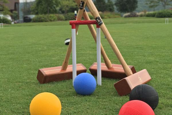 4 croquet balls on the grass and 3 croquet mallets leaning against a wicket