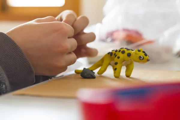 Hands molding yellow clay into animal.