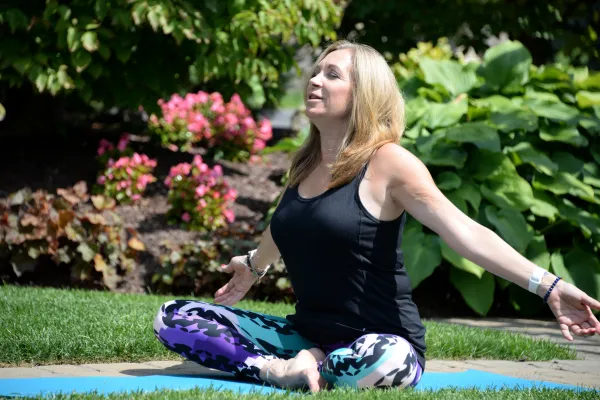 Woman sitting outside doing yoga with her arms stretched out wide