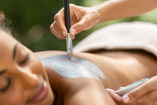 Mud being painted on woman's back for spa treatment.