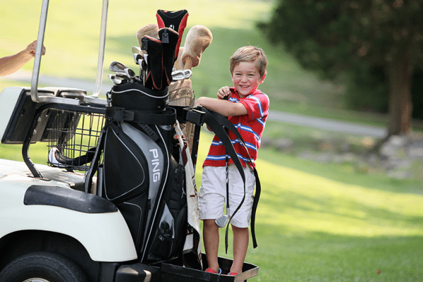 Little boy standing on the back of a golf cart