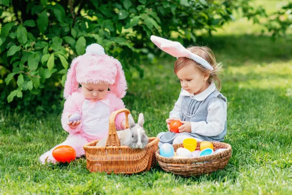 Two very young children dressed up in bunny outfits playing with eggs.