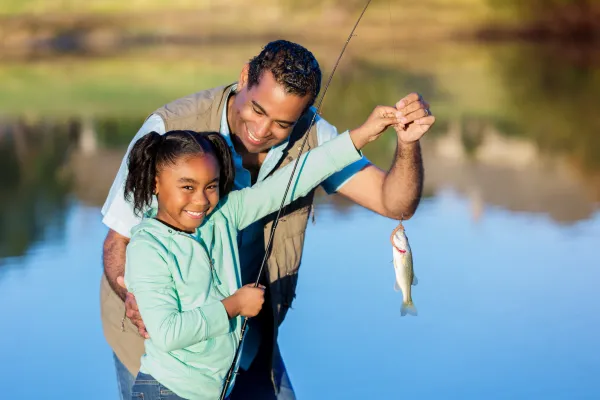 Young girl and older gentleman holding a fish at a pond.