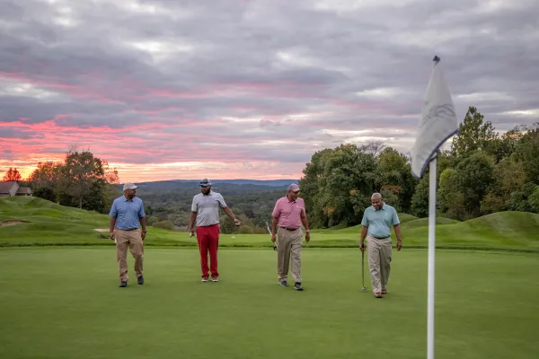 Guys foursome walking on a golf course with the sunset in the background