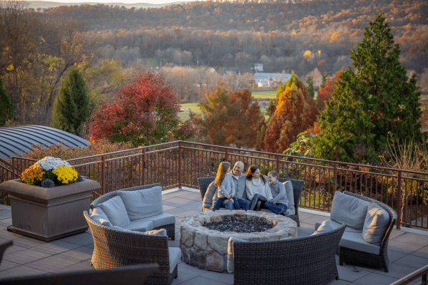 Family of 4 sitting by firepit on fire &amp; water terrace with fall background.