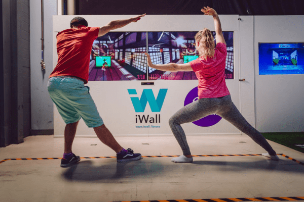 Two people working out in front of iwall machine.