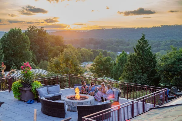 Group of four girlfriends sitting around firepit on Fire &amp; Water terrace overlooking sunset mountain views.