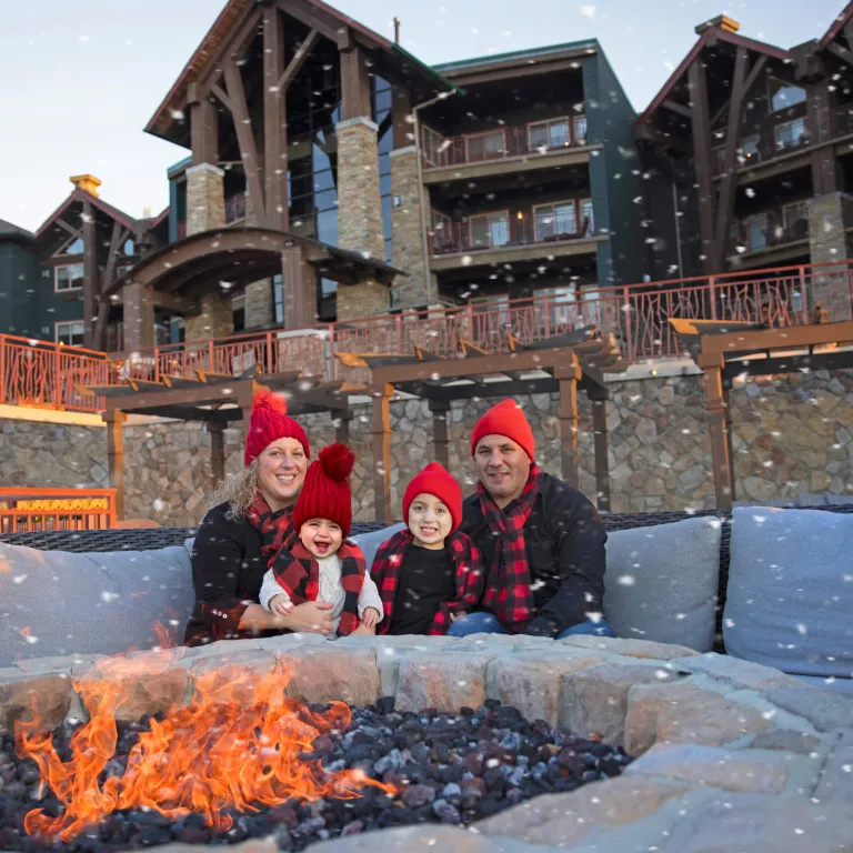 Family of four sits around firepit as it snows around them on Fire & Water Terrace