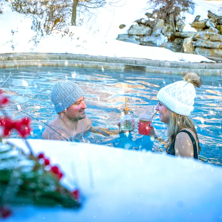 Couple drinks cocktails in outdoor snow pool.