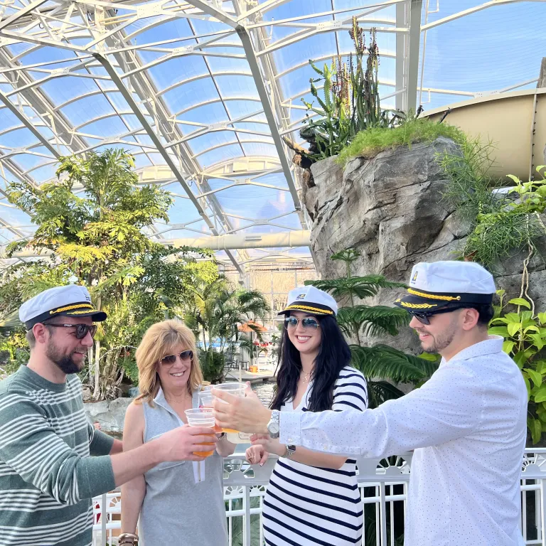 Four people stand with captain hats in Biosphere pool cheersing their drinks.