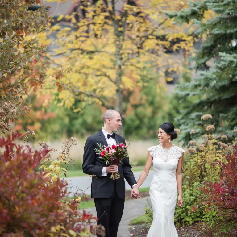 Bride and groom holding hands walking through fall path.