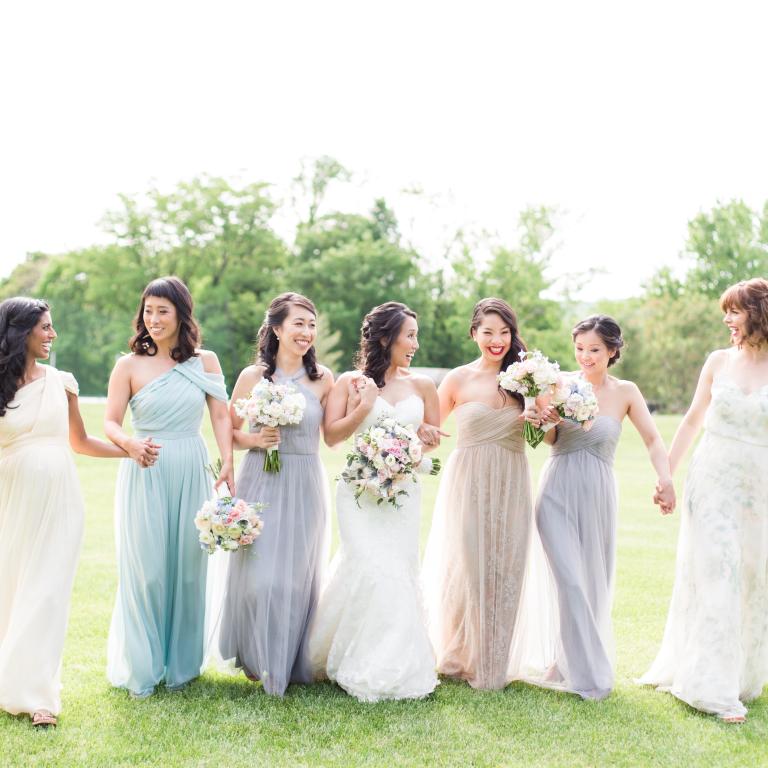 Bridesmaids and bride walk through grass field.