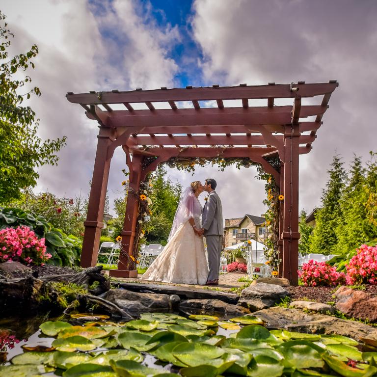 Bride and groom kiss under ceremony arch.