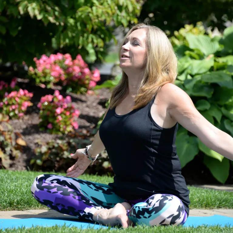 Woman sitting outside doing yoga with her arms stretched out wide