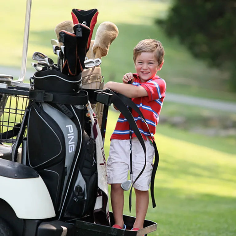 Little boy standing on the back of a golf cart