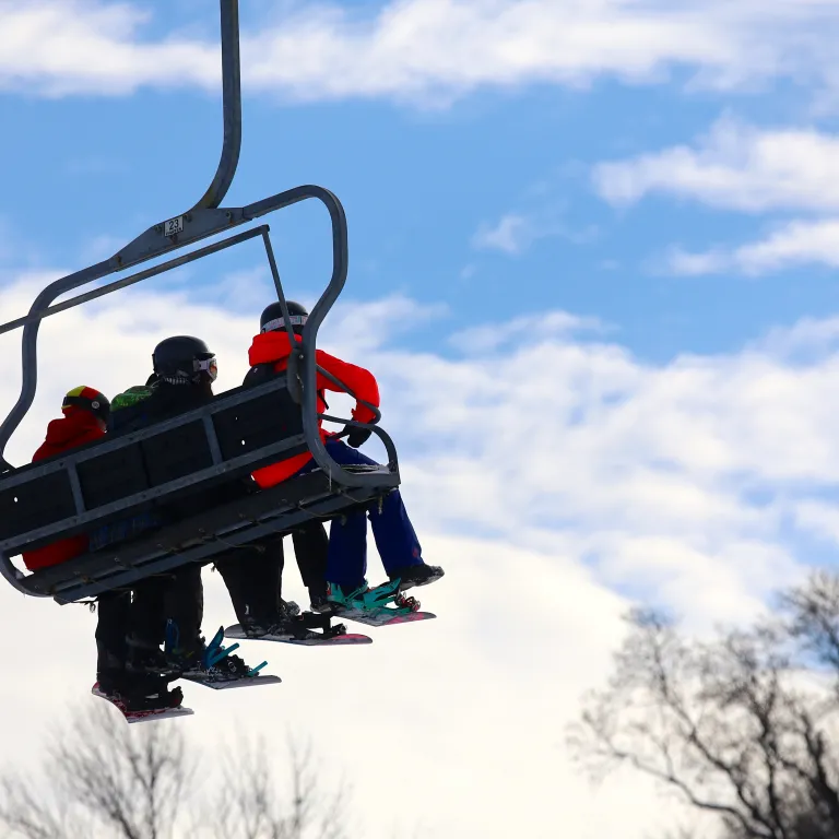 Three people sitting on ski lift.