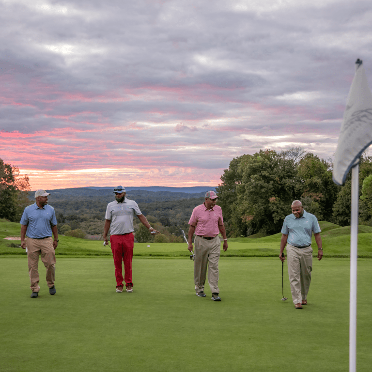 Guys foursome walking on a golf course with the sunset in the background