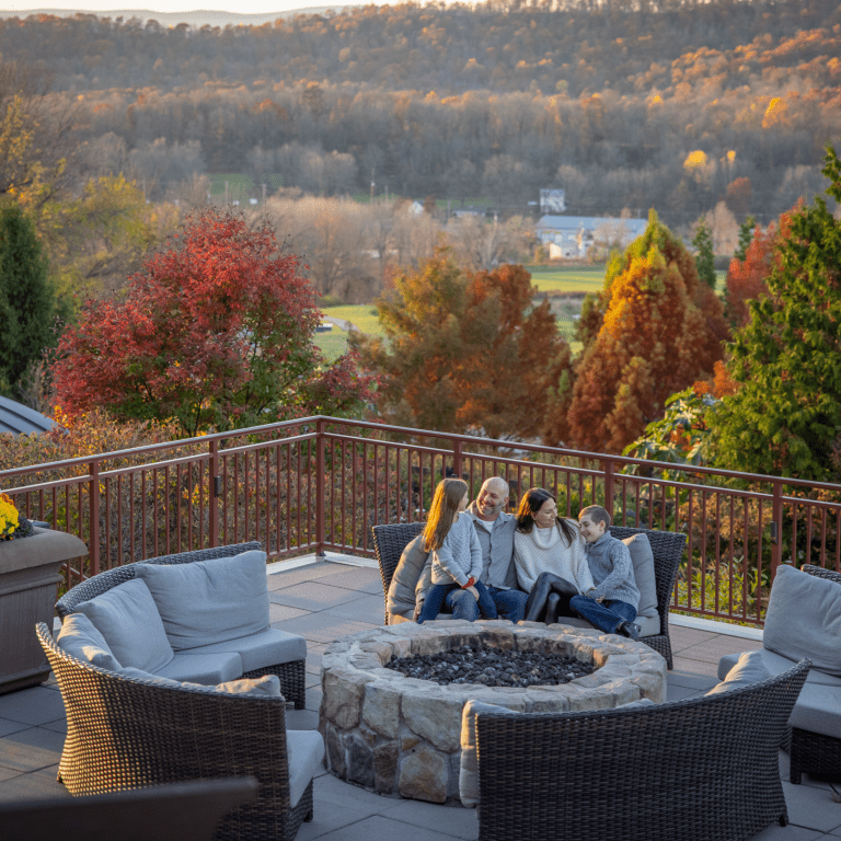 Family of 4 sitting by firepit on fire &amp; water terrace with fall background.