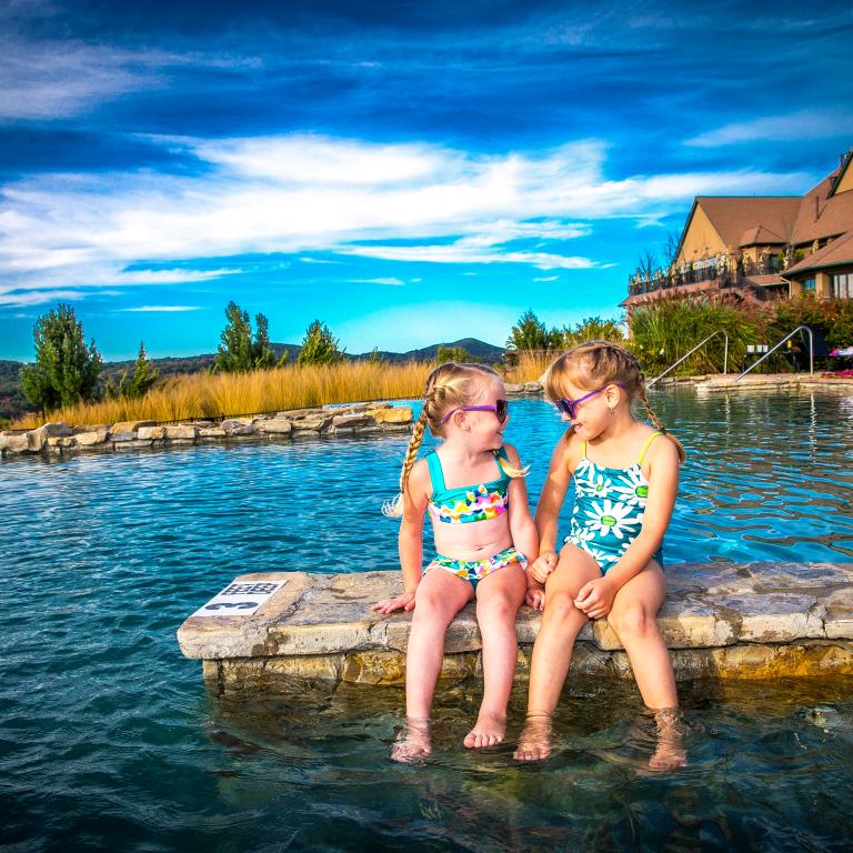 Two young girls wearing sunglasses and sitting at the Vista 180 pool.