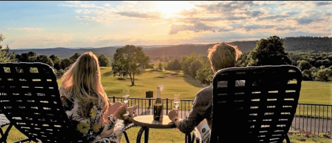 Couple sitting in lounge chairs at vista 180 pool looking towards the sunset and mountains.