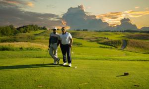 Two golfers stand on Ballyowen Golf Course with sunset behind them. 