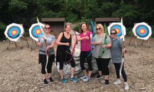 Five girlfriends holding bows at archery range. 