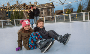 Kids sitting on glice skating rink.