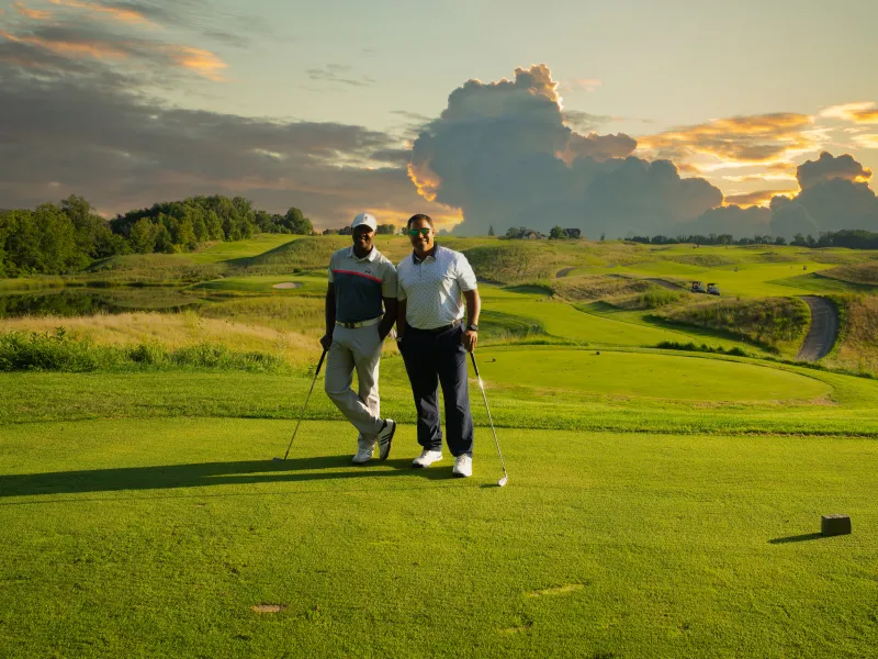 Two golfers stand on Ballyowen Golf Course with sunset behind them. 