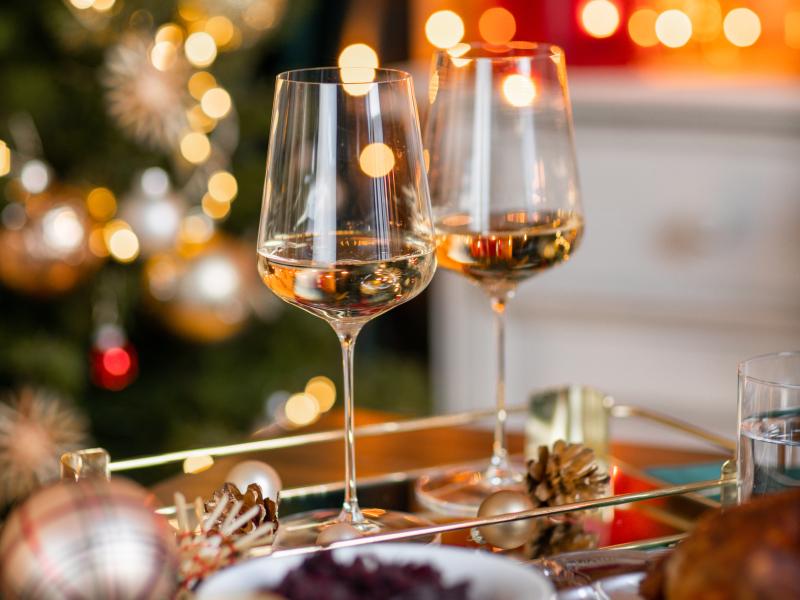 2 wine glasses with holiday lights and decorations in background