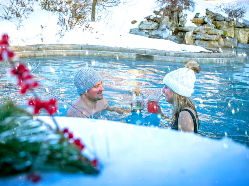 Couple drinks cocktails in outdoor snow pool.