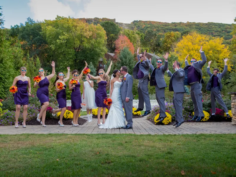 Bride and groom kissing while their wedding party jumps in air.