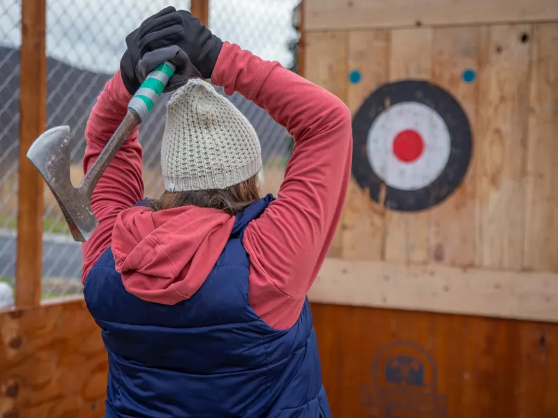 Woman wearing hat and gloves getting ready to throw axe at target.