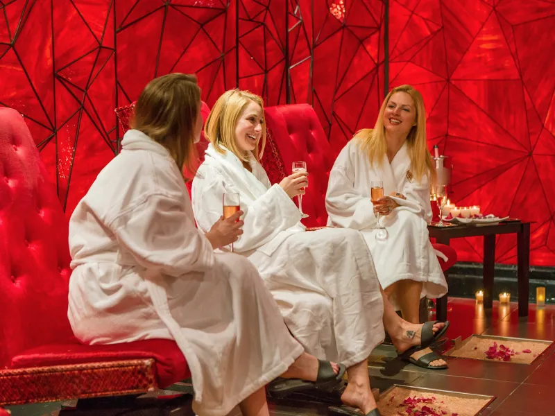 Group of girlfriends in white robes drinking champagne in Reflections Spa's Crystal Room.