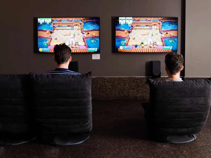 Two children sitting in front of two tvs playing video games.