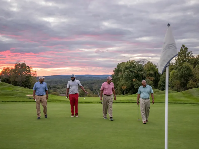 Guys foursome walking on a golf course with the sunset in the background