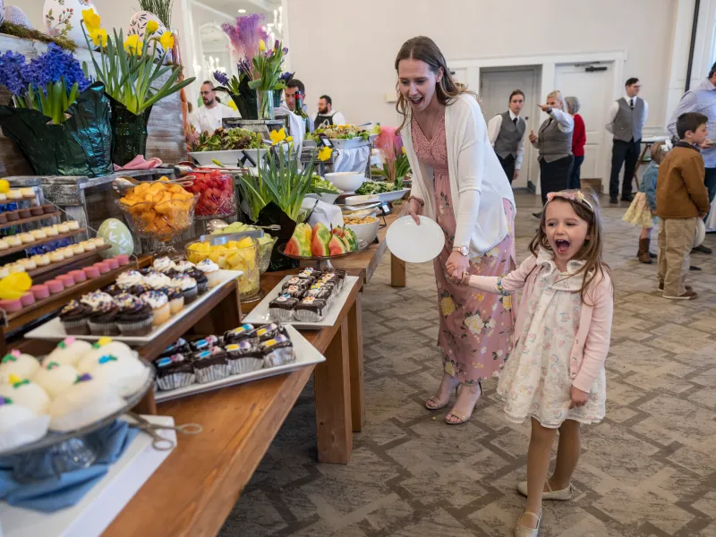 Woman and child holding hands and looking at buffet of food. 